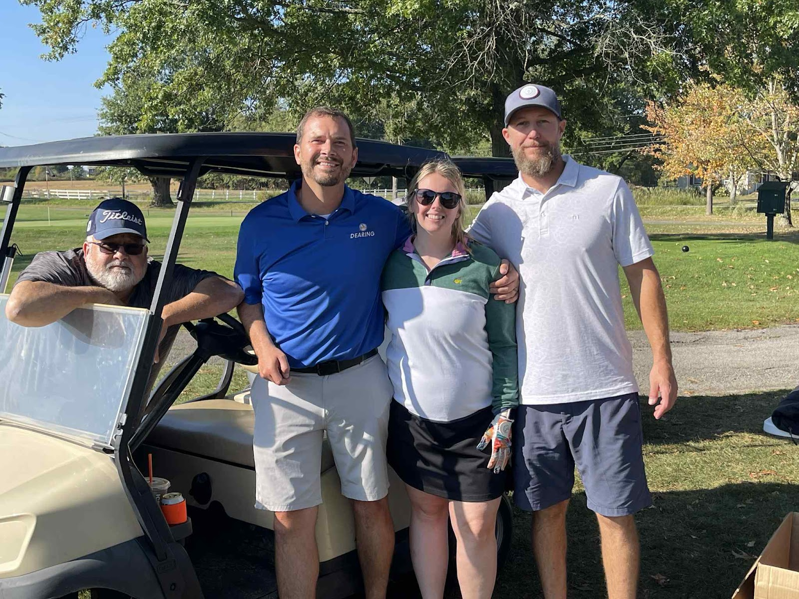 Group of four participants posing together by a golf cart during the annual company golf outing.