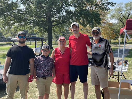 Five golfers smiling together in front of a golf cart at the annual company outing.