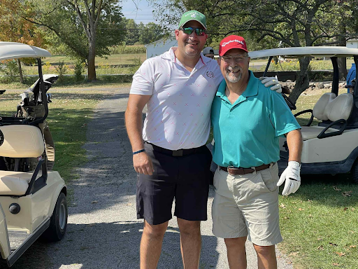 Two golfers smiling together in front of a golf cart at the annual company outing.