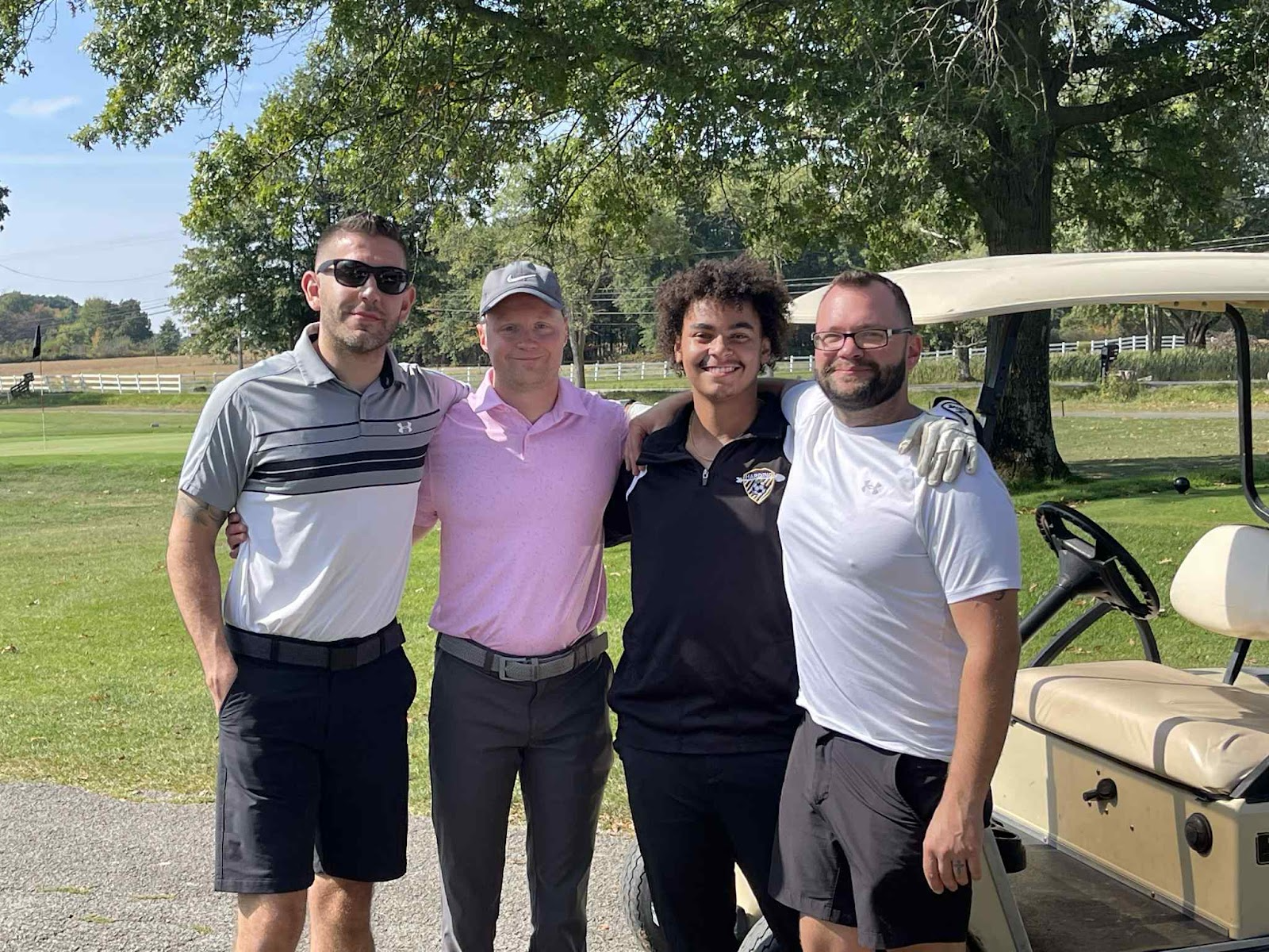 Four golfers smiling together in front of a golf cart at the annual company outing.