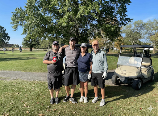 Four golfers smiling together in front of a golf cart at the annual company outing.
