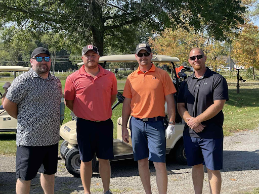 Four golfers smiling together in front of a golf cart at the annual company outing.