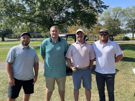 Four golfers smiling together in front of a golf cart at the annual company outing.